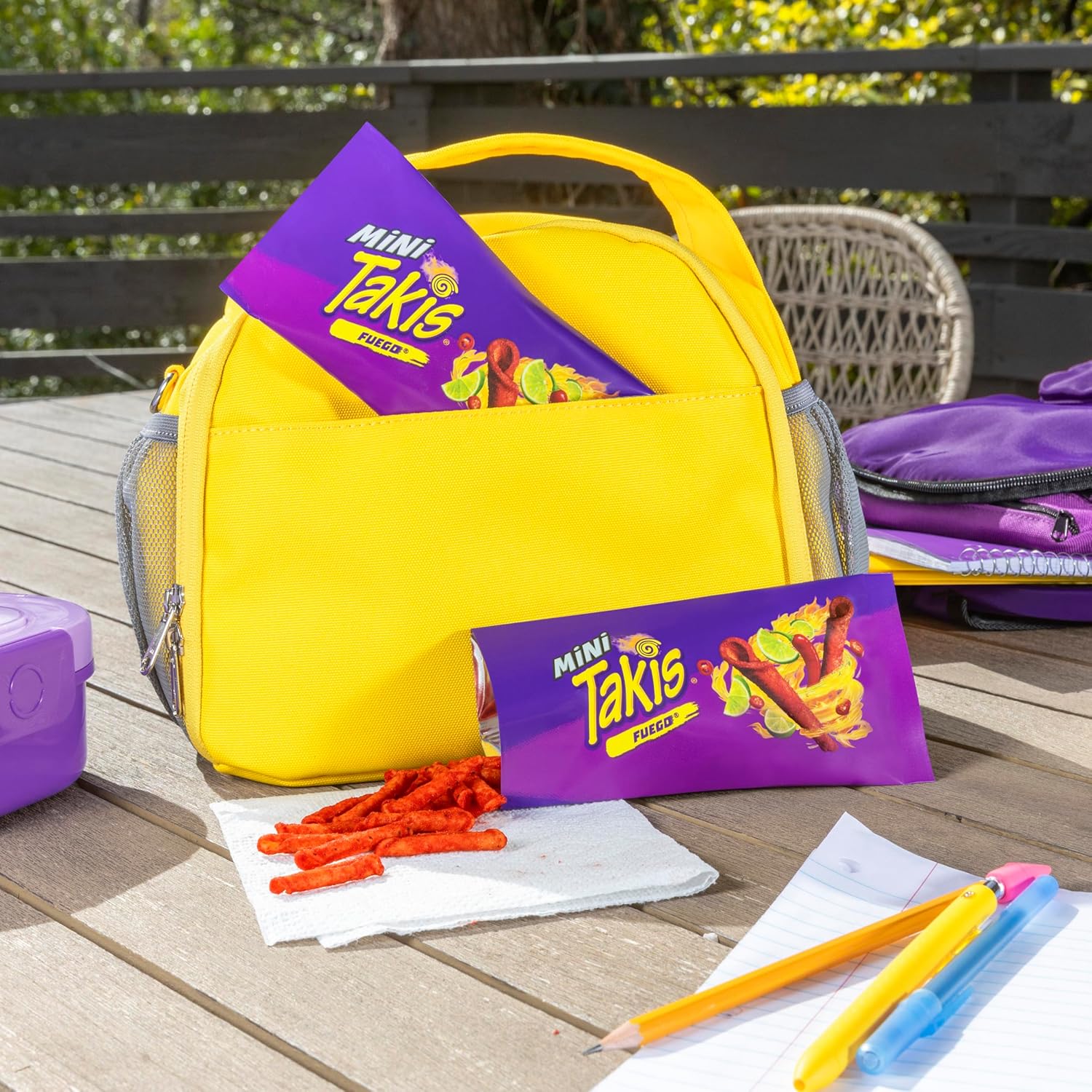 Yellow lunch bag with Mini Takis packaging on a wooden table outdoors.